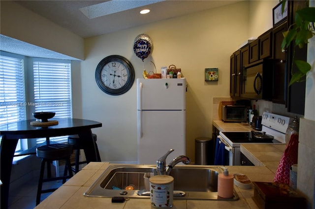 kitchen featuring sink, tile countertops, a textured ceiling, white appliances, and dark brown cabinets