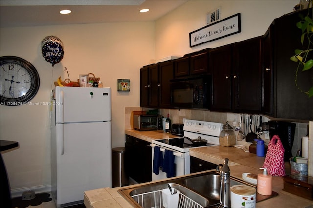 kitchen featuring vaulted ceiling, tile counters, white appliances, and sink