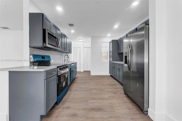 kitchen featuring light wood-type flooring, tasteful backsplash, stainless steel appliances, sink, and gray cabinets