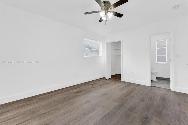 unfurnished bedroom featuring ceiling fan, dark wood-type flooring, a spacious closet, connected bathroom, and a closet