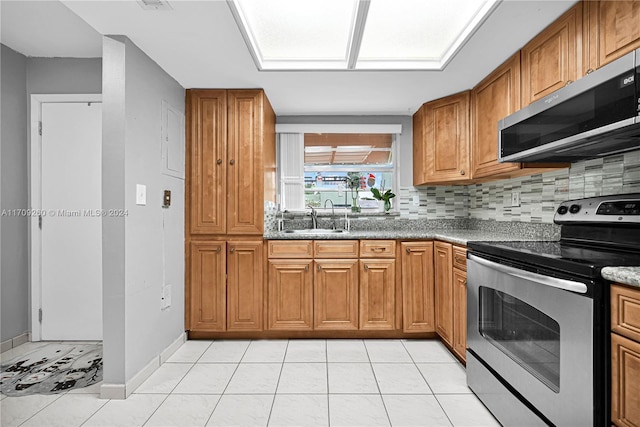 kitchen featuring light stone countertops, appliances with stainless steel finishes, backsplash, sink, and light tile patterned floors