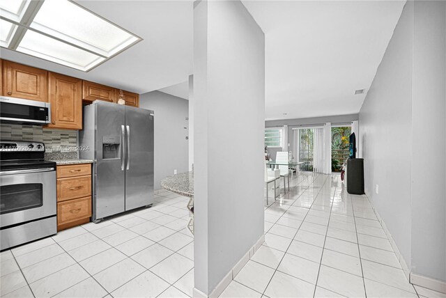 kitchen featuring decorative backsplash, light tile patterned flooring, light stone countertops, and appliances with stainless steel finishes