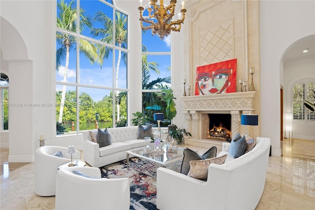 living room with an inviting chandelier, a towering ceiling, a high end fireplace, and crown molding