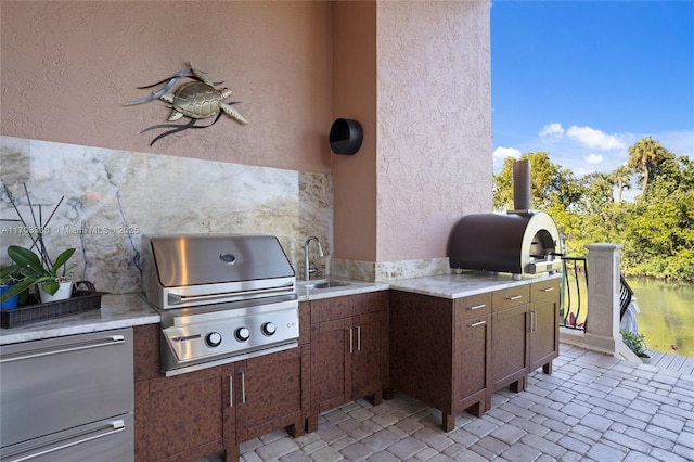 view of patio with exterior kitchen, a water view, a grill, and sink