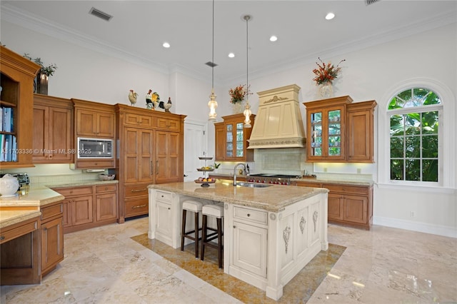 kitchen with a breakfast bar area, custom range hood, pendant lighting, stainless steel appliances, and a kitchen island with sink