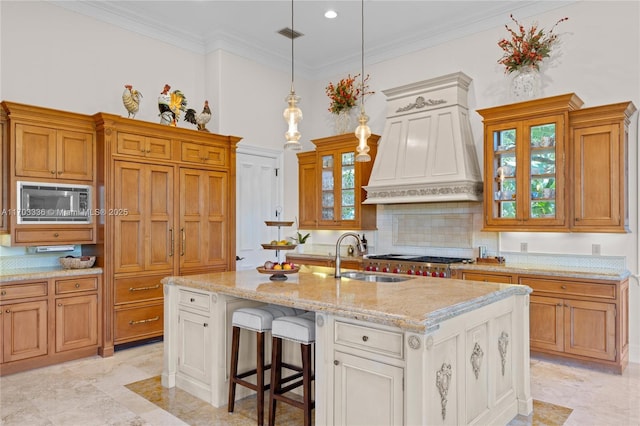 kitchen with premium range hood, built in microwave, ornamental molding, a kitchen island with sink, and white cabinets