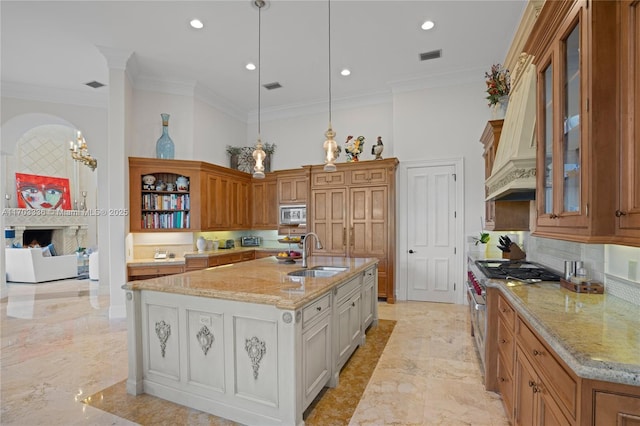 kitchen with sink, light stone counters, decorative light fixtures, a kitchen island with sink, and white cabinets