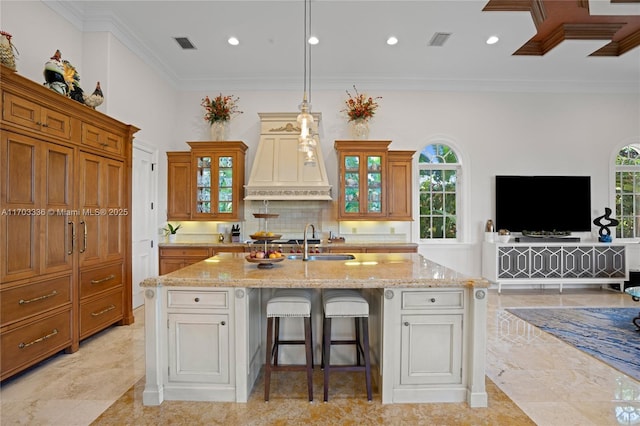 kitchen featuring sink, a breakfast bar area, a kitchen island with sink, ornamental molding, and light stone countertops