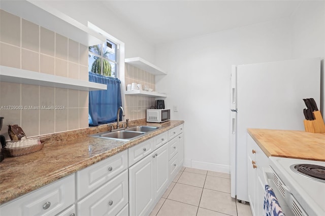 kitchen with white appliances, backsplash, sink, light tile patterned floors, and white cabinetry