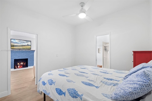 bedroom featuring connected bathroom, ceiling fan, a fireplace, and wood-type flooring