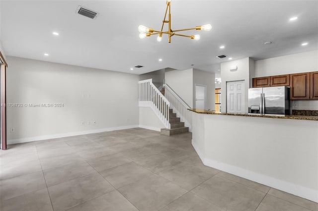 kitchen with dark stone counters, an inviting chandelier, stainless steel fridge, decorative light fixtures, and light tile patterned flooring