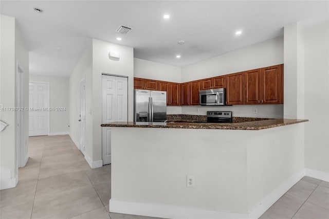 kitchen featuring dark stone countertops, kitchen peninsula, light tile patterned floors, and stainless steel appliances