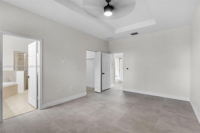 unfurnished bedroom with a closet, a tray ceiling, ensuite bath, and ceiling fan