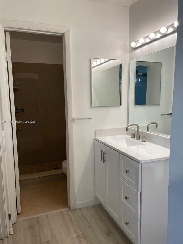 bathroom with hardwood / wood-style flooring, toilet, walk in shower, and vanity