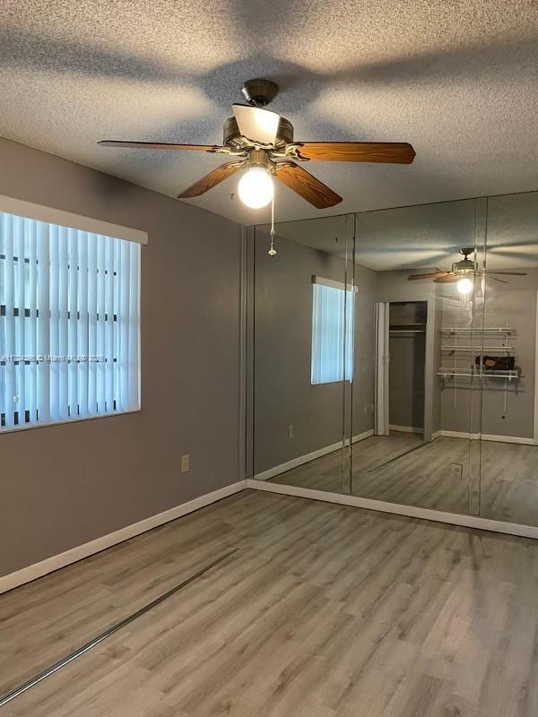 unfurnished bedroom featuring ceiling fan, a textured ceiling, a closet, and hardwood / wood-style floors