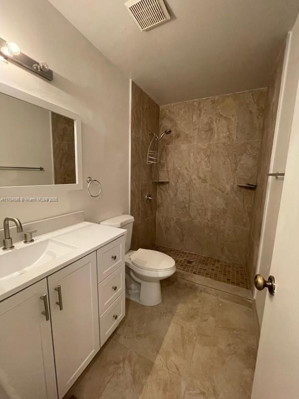 bathroom featuring toilet, vanity, and a tile shower