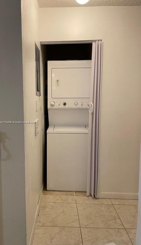 washroom with stacked washing maching and dryer, a textured ceiling, and light tile patterned flooring