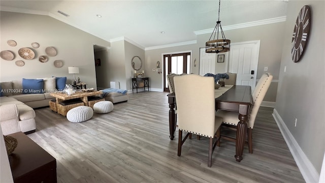 dining space with hardwood / wood-style flooring, a chandelier, crown molding, and vaulted ceiling