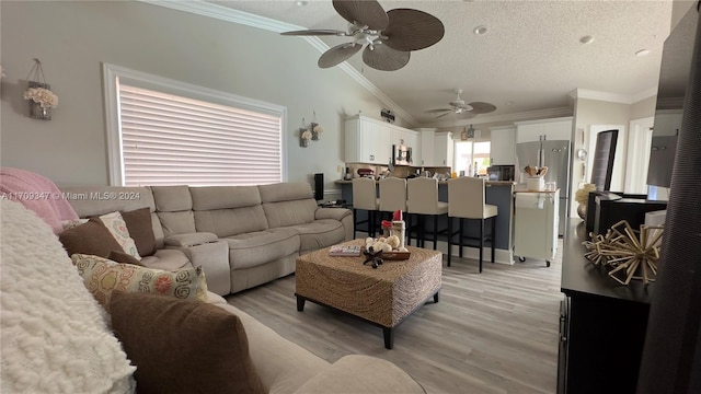 living room with light wood-type flooring, ornamental molding, a textured ceiling, vaulted ceiling, and ceiling fan