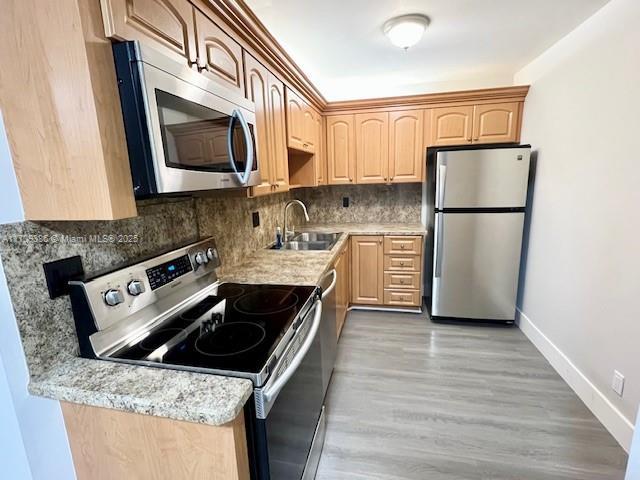 kitchen with light stone counters, light brown cabinetry, sink, and appliances with stainless steel finishes