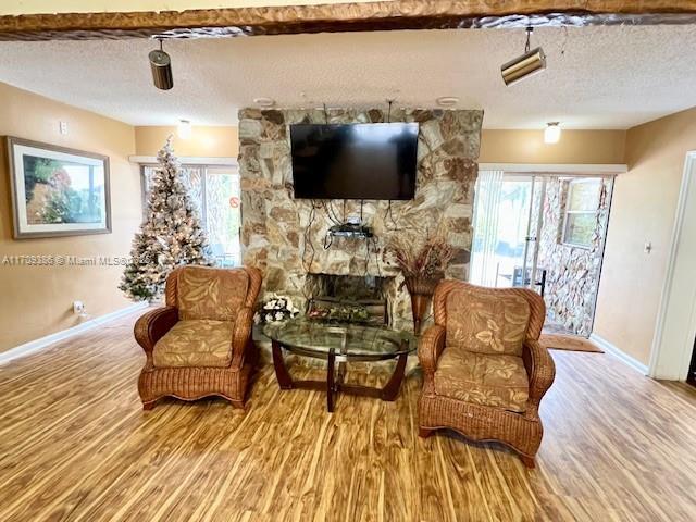 living area featuring a textured ceiling, light hardwood / wood-style floors, and a stone fireplace