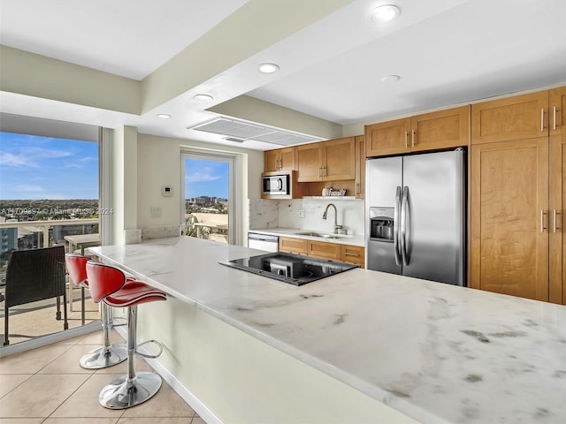 kitchen featuring a kitchen bar, tasteful backsplash, stainless steel appliances, sink, and light tile patterned floors