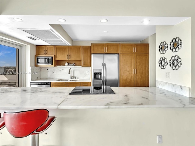 kitchen featuring sink, stainless steel appliances, backsplash, kitchen peninsula, and a breakfast bar