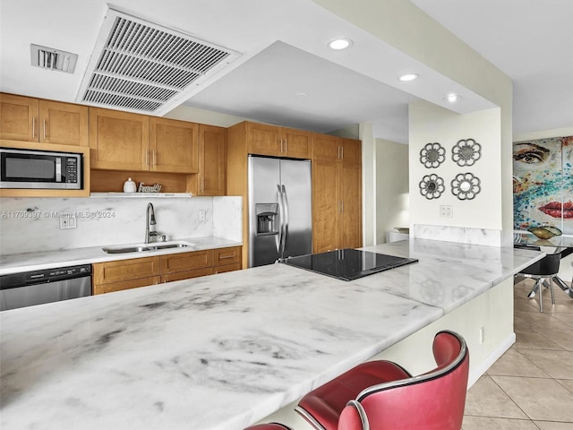 kitchen with kitchen peninsula, a kitchen breakfast bar, stainless steel appliances, sink, and light tile patterned floors