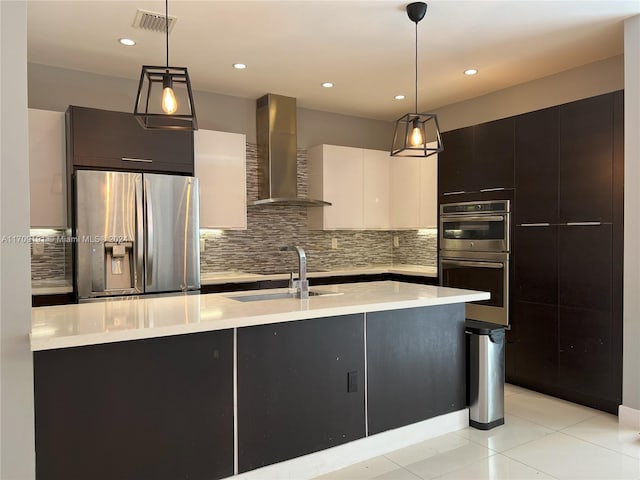 kitchen featuring stainless steel appliances, wall chimney range hood, pendant lighting, a center island with sink, and white cabinets