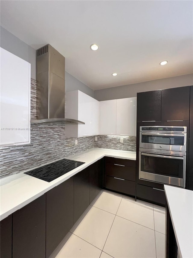 kitchen featuring stainless steel double oven, wall chimney range hood, decorative backsplash, black electric stovetop, and white cabinets