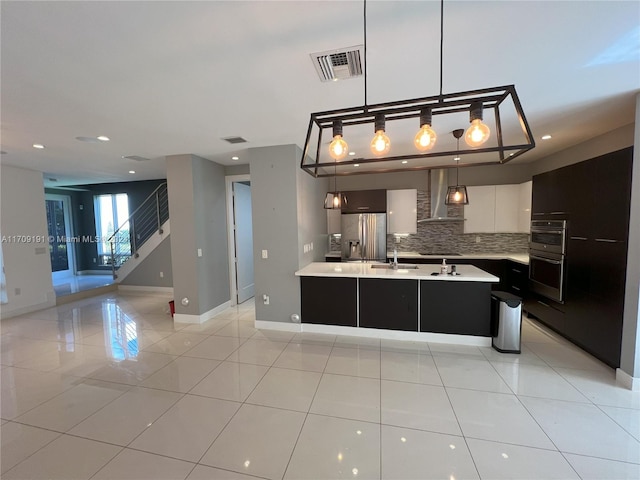 kitchen featuring backsplash, wall chimney range hood, appliances with stainless steel finishes, decorative light fixtures, and white cabinetry