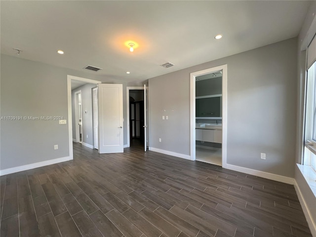 unfurnished bedroom featuring multiple windows, ensuite bathroom, and dark hardwood / wood-style floors