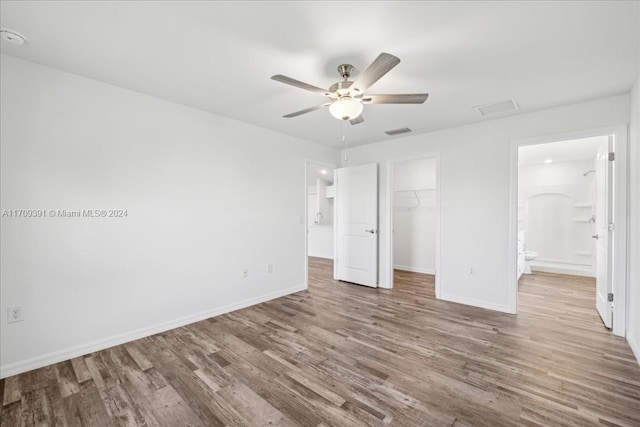 unfurnished bedroom with a walk in closet, ceiling fan, wood-type flooring, connected bathroom, and a closet