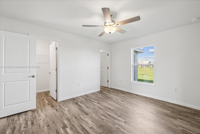 unfurnished bedroom with ceiling fan, light hardwood / wood-style floors, a walk in closet, and a closet