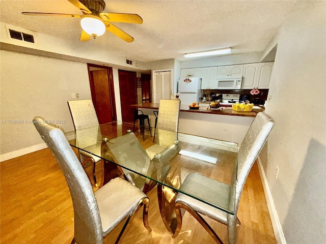 dining area with light wood-type flooring, ceiling fan, and a textured ceiling