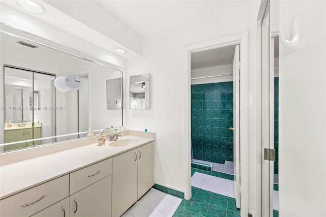 bathroom featuring tile patterned flooring, a tile shower, and vanity