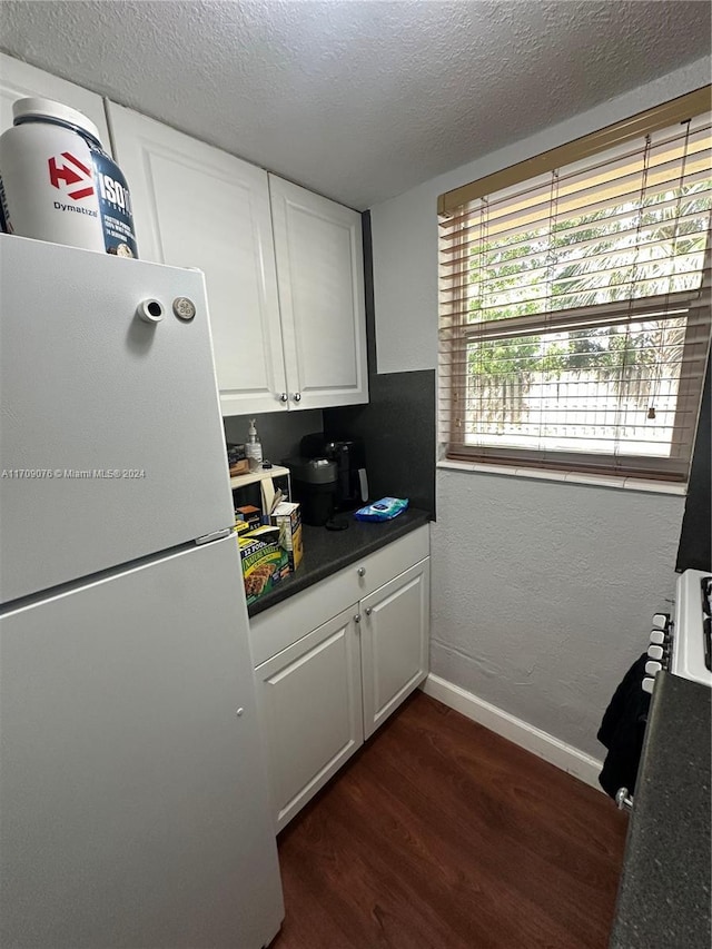 kitchen with a textured ceiling, white cabinetry, white fridge, and dark hardwood / wood-style floors