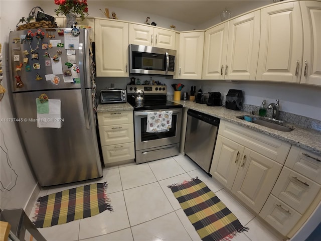 kitchen featuring light stone counters, sink, light tile patterned floors, and stainless steel appliances