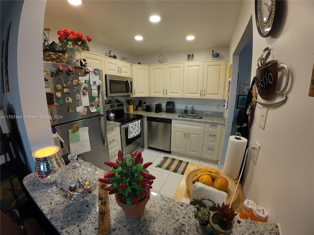 kitchen with sink, light stone countertops, light tile patterned floors, appliances with stainless steel finishes, and white cabinetry