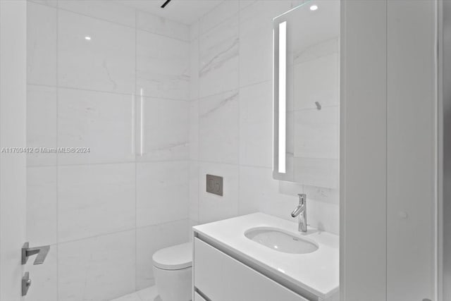 bathroom with vanity, tile walls, and toilet