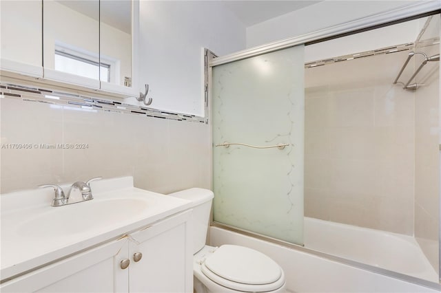 full bathroom featuring shower / bath combination with glass door, vanity, tile walls, and toilet