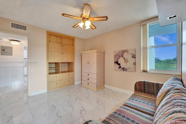 living area featuring electric panel, ceiling fan, and a textured ceiling