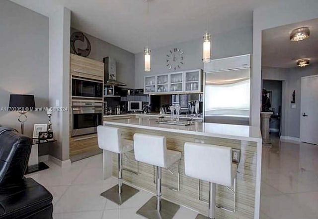 kitchen featuring built in appliances, decorative light fixtures, and wall chimney range hood