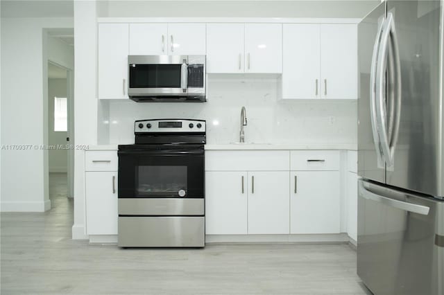 kitchen featuring backsplash, sink, light hardwood / wood-style flooring, appliances with stainless steel finishes, and white cabinetry