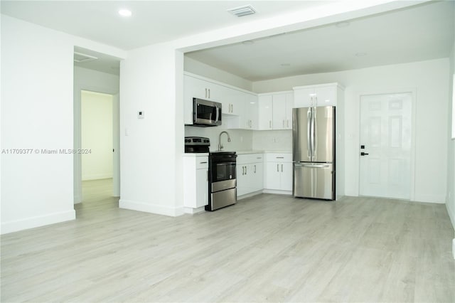 kitchen with backsplash, stainless steel appliances, white cabinetry, and light hardwood / wood-style floors