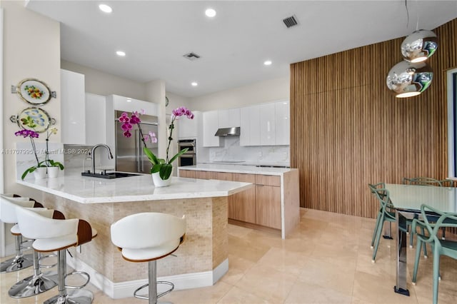 kitchen with kitchen peninsula, tasteful backsplash, a breakfast bar, sink, and white cabinets