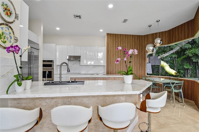 kitchen featuring sink, backsplash, white cabinets, decorative light fixtures, and stainless steel double oven