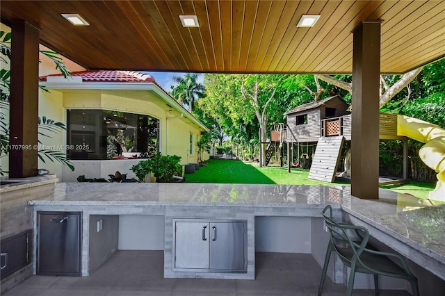 view of patio / terrace with exterior bar, a playground, and an outdoor kitchen