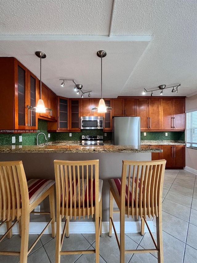 kitchen with decorative light fixtures, light tile patterned floors, kitchen peninsula, and appliances with stainless steel finishes