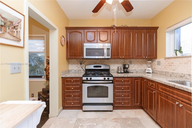 kitchen with white gas stove, ceiling fan, light stone counters, and backsplash